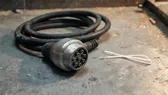 Konektor logam multi-pin dengan gulungan kabel karet tebal di lantai beton bengkel usang, beberapa cable tie putih di dekatnya