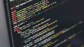 Layar monitor menampilkan kode sumber dengan pewarnaan sintaks di atas latar gelap